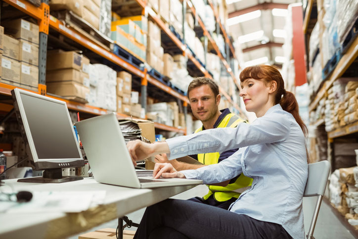 warehouse manager and worker looking at laptop in warehouse