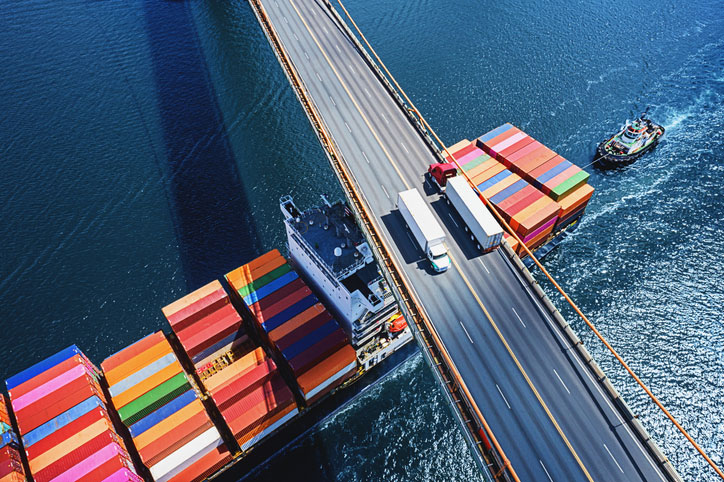 trucks on bridge with container ships below